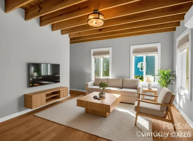 Open-concept living space featuring warm wood flooring, exposed beam ceilings, and abundant natural light flowing into the modern kitchen.