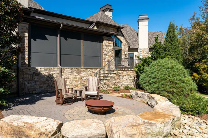 A lower paver terrace with a sculptural gas fire bowl and boulder seating creates an intimate setting amid the privacy of the wooded landscape