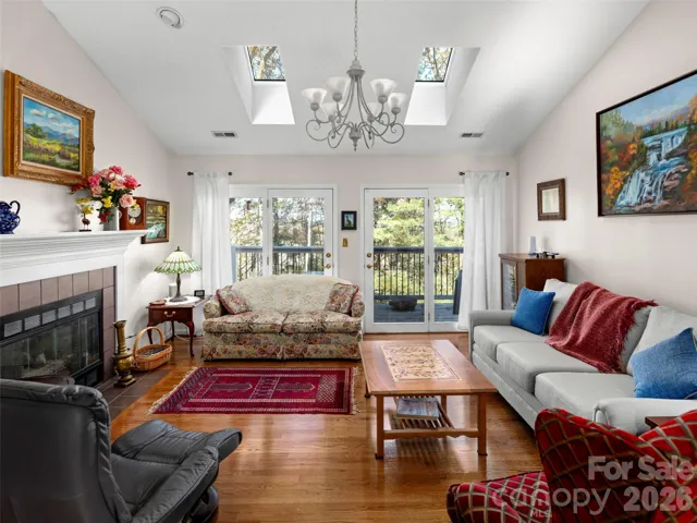 An inviting living room with hardwood floors, a gas fireplace, and skylights offers abundant natural light, while double doors provide easy access to the rear deck, enhancing indoor-outdoor flow.