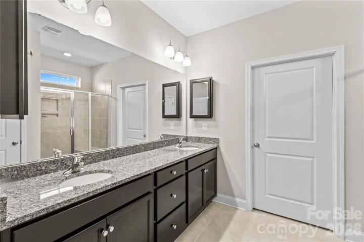 Primary bath with ebony cabinets, granite dual sinks and tile flooring