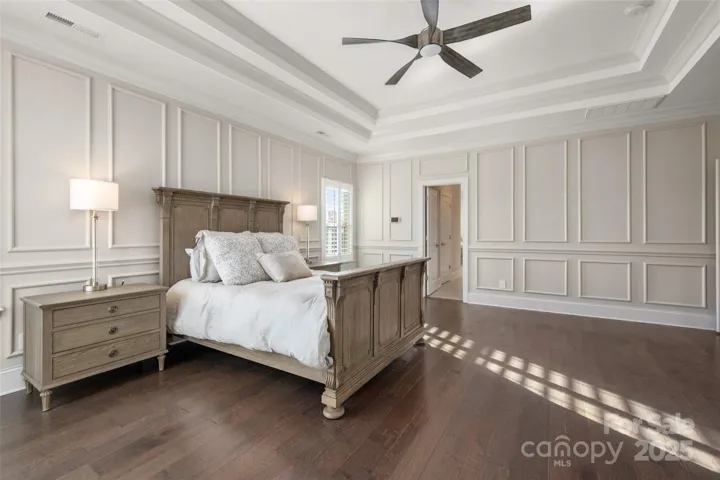 Primary bedroom with custom trim detail, hardwood flooring and multiple treyed ceiling