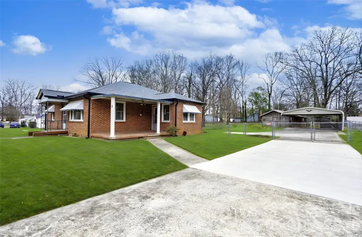 Home with driveway, gated fenced driveway, outbuilding, and two car covered space.