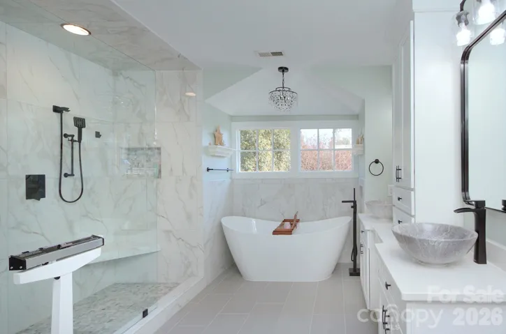 The luxurious primary bath includes a freestanding soaking tub and oversized glass shower wrapped in elegant marble-style tile.