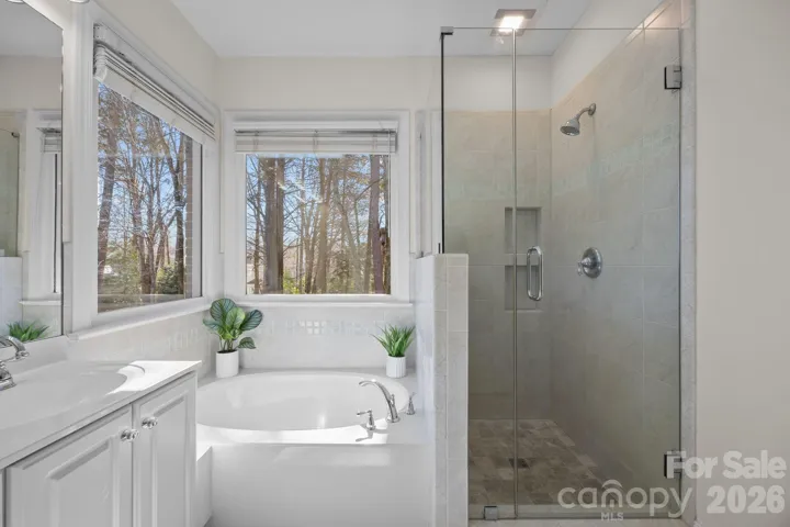 It features a contemporary free-standing shower, enclosed in glass, offering a clean, modern aesthetic, a dual vanity with ample counter space and storage, perfect for morning routines, a beautiful garden tub—ideal for soaking— strategically placed to serve as an attractive focal point and a private water closet, separated by a door.