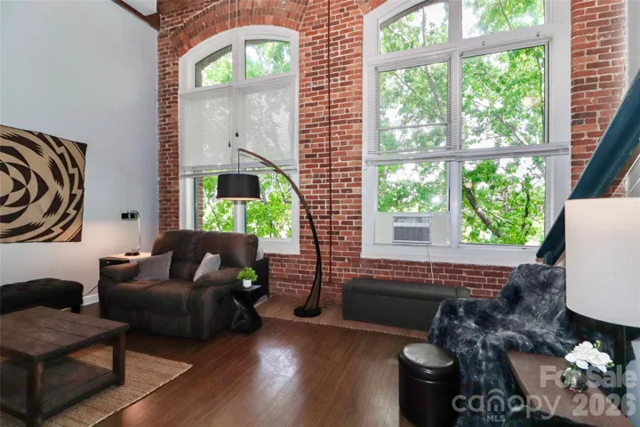 The living room boasts oversized industrial windows, flooding the room with natural light.