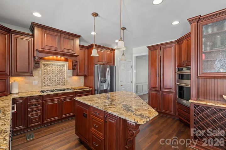Beautiful granite and tile backsplash compliment the custom hood over the gas range cooktop.
