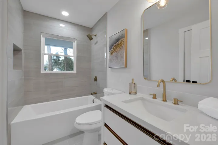 Full Bathroom – Stylishly renovated bath with tiled tub/shower surround, sleek gold fixtures, modern vanity, and contemporary lighting.