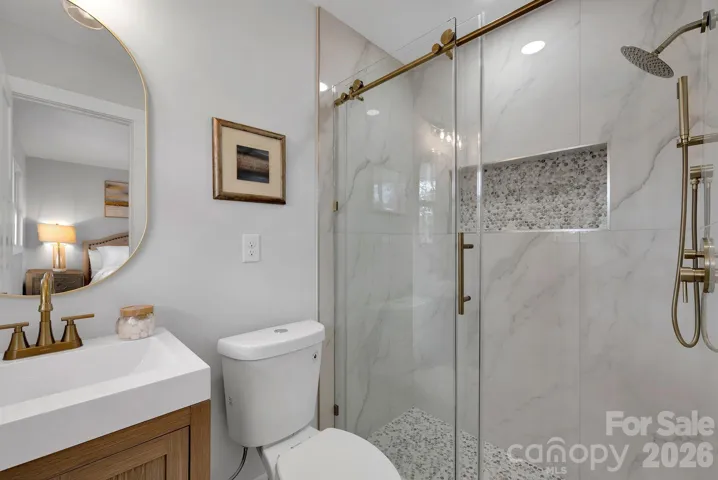 Primary Bathroom – Beautifully updated bath featuring a glass-enclosed walk-in shower with marble-style tile, pebble accent niche, and modern gold fixtures.