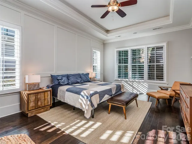 Main Floor Primary Suite with Wood Flooring, Extensive Molding, Built-In Audio, Tray Ceiling, & Plantation Blinds.