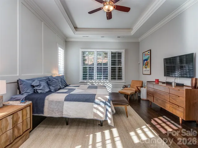 Main Floor Primary Suite with Wood Flooring, Extensive Molding, Built-In Audio, Tray Ceiling, & Plantation Blinds.