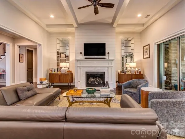 The Open Great Room Features Coffered Ceiling, Wood Floors, Shiplap Entertainment Wall, Gas Log Fireplace, & Access to the Screened Porch & Gourmet Kitchen