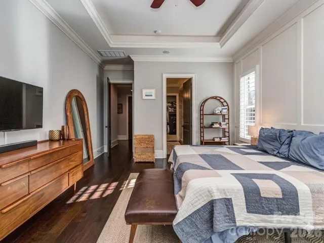 Main Floor Primary Suite with Wood Flooring, Extensive Molding, Built-In Audio, Tray Ceiling, & Plantation Blinds.