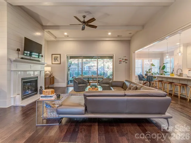 The Open Great Room Features Coffered Ceiling, Wood Floors, Shiplap Entertainment Wall, Gas Log Fireplace, & Access to the Screened Porch & Gourmet Kitchen