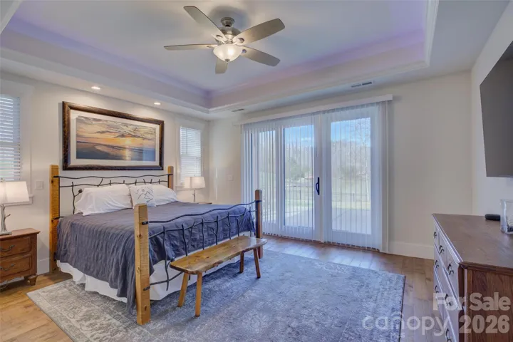 Primary Bedroom with tray ceiling, fan with light, hardwood floors, and waterview