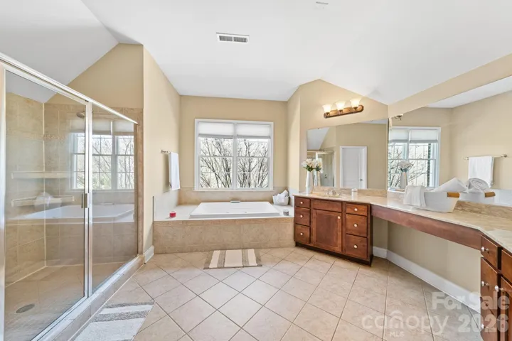 Spa-like primary bath featuring dual vanities, a soaking tub beneath large windows, and a glass-enclosed walk-in shower for the ultimate relaxation experience.
