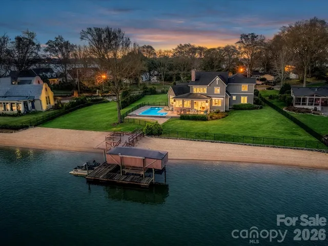 Twilight aerial view showcasing a stunning waterfront residence with a private dock, sandy shoreline, and resort-style pool overlooking the tranquil waters of Lake Norman.