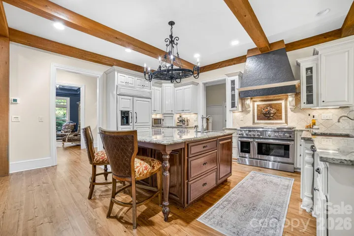 The Chef’s kitchen boasts a large island with vegetable sink and bar stool seating at the island and counter, a custom backsplash with bronze artwork and limestone tile. The Kitchen sink is hammered copper with a reverse osmosis system. The GE Monogram double oven with 6 burner gas stove & griddle has a Dacor commercial hood vent.