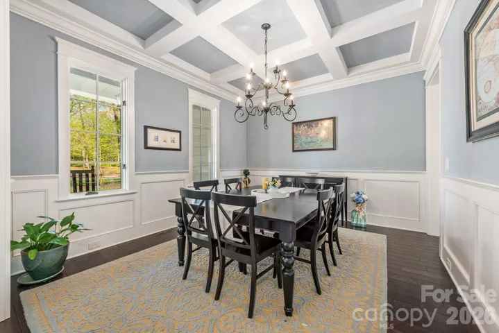 Dining room with unique coffered ceiling and elegant wainscotting detail. Windows and doors include pediment casing