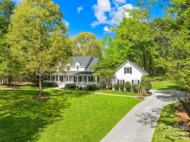 Charming farmhouse-style home on a lush, tree-lined lot with a welcoming wraparound porch and peaceful, private setting.