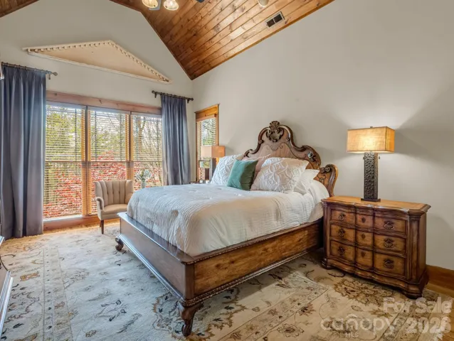 Exquisite primary suite includes vast windows, screened porch access and vaulted wood planked ceiling.