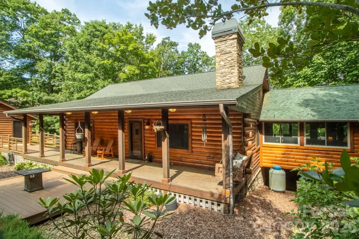 Front Exterior – Right PerspectiveBeautifully maintained log home featuring a striking stone chimney, covered front porch, and lush landscaping that blends naturally with the wooded setting.