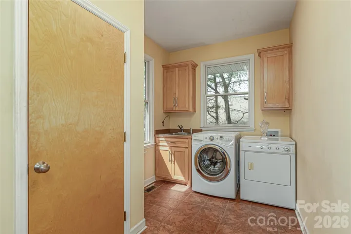 Separate laundry/mudroom entry with coat closet, tile flooring, ample cabinetry, and a utility sink.