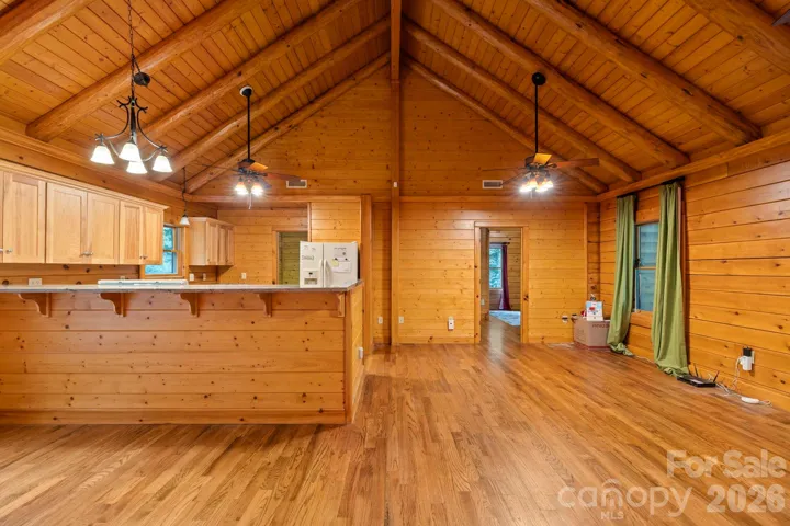 Open-concept living area featuring vaulted ceilings, exposed wood beams, and hardwood floors, creating a warm and inviting gathering space.