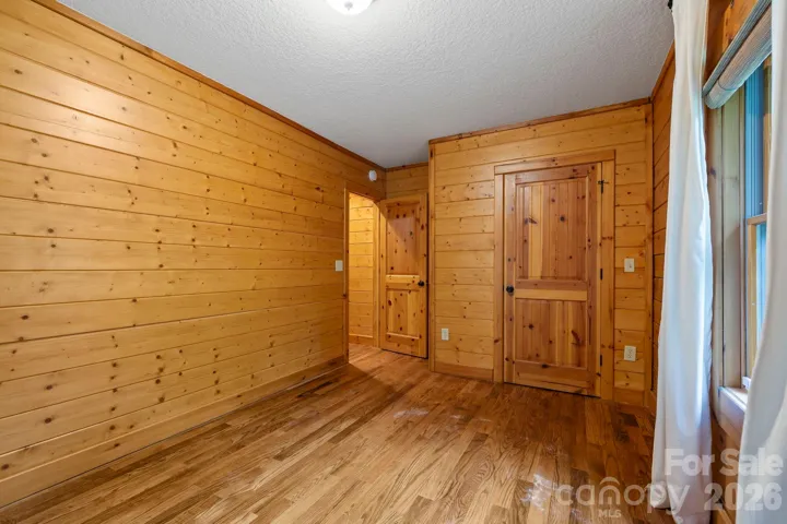 Cozy bedroom featuring warm wood-paneled walls, hardwood floors, and abundant natural light for a true mountain retreat feel.