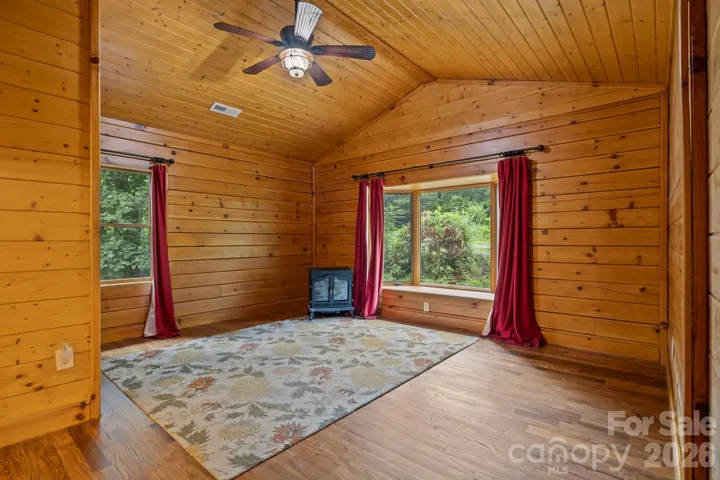 Comfortable bedroom with wood-paneled walls, large windows, and a cozy stove feature adding character and warmth.