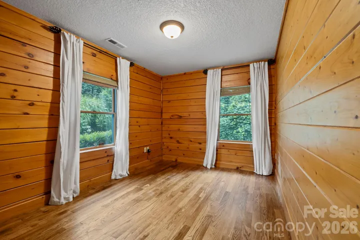 Cozy bedroom featuring wood accent walls and a window overlooking the surrounding greenery.