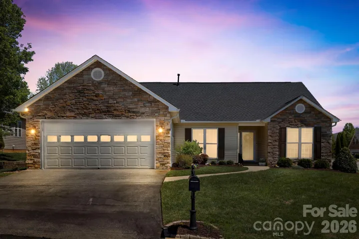 Inviting curb appeal with a stone-accented façade, two-car garage, and soft exterior lighting that highlights the home at dusk.