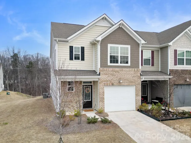 Classic brick and hardboard siding townhome in sought-after Windhaven, Tega Cay. Charming curb appeal with a welcoming front door, manicured entry, and attached garage — all under a Carolina blue sky.