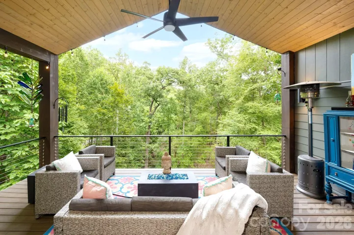 Outdoor living space with vaulted ceiling, fan, and treetop views.