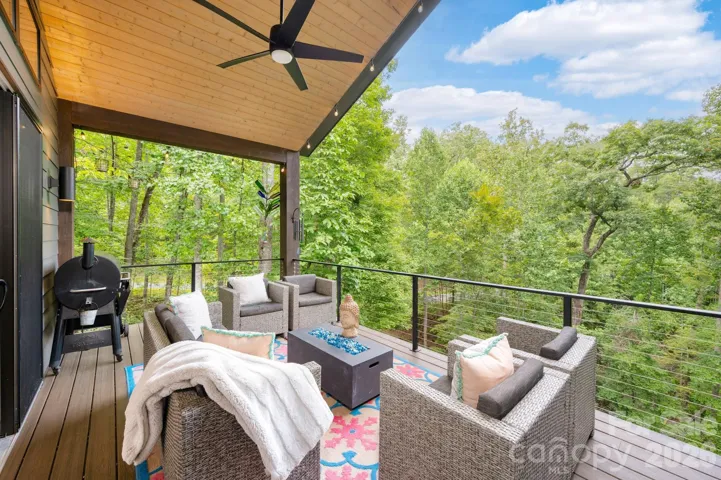 Covered deck with seating and grilling area, overlooking lush forest.