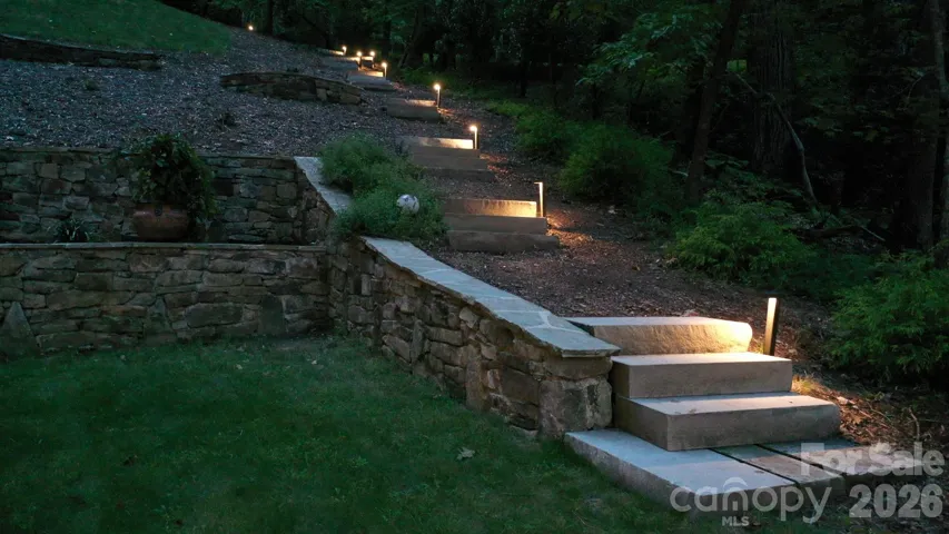 Terraced stone landscaping with illuminated pathway steps leading into the forest.