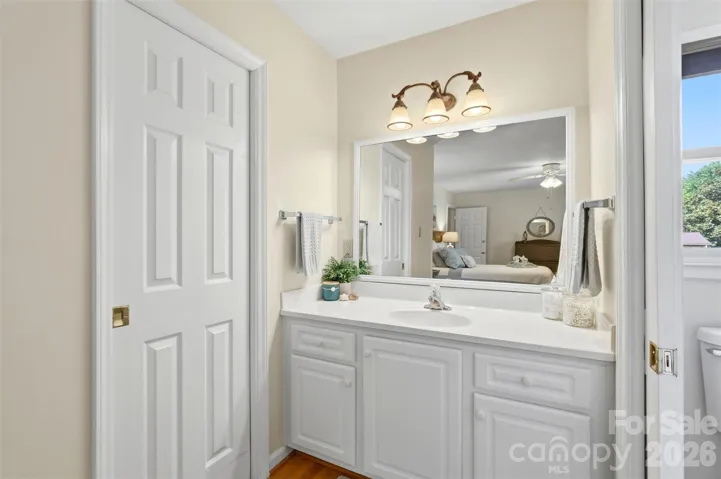 Primary vanity with lots of light is located between the walk in closet and the shower room