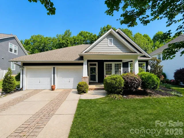 Charming single-story home with a welcoming front porch, two-car garage, and beautifully maintained landscaping, all set beneath mature trees in a peaceful neighborhood.