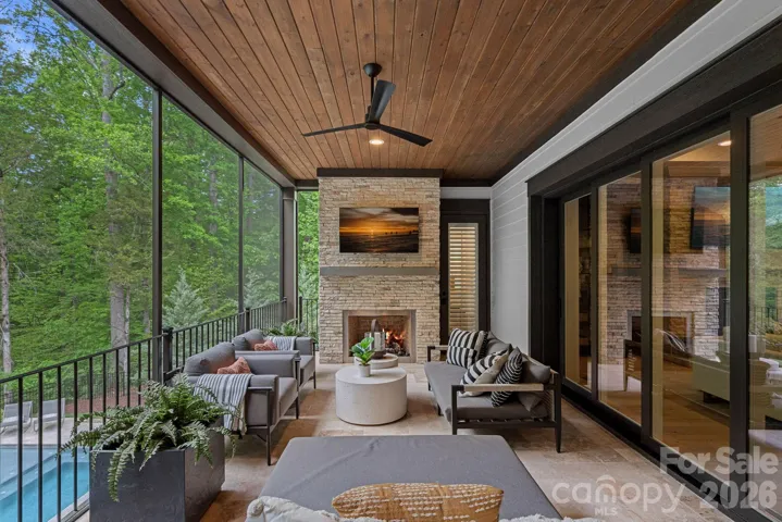 Outdoor living soace completed with a gas fireplace, TV and view of the pool.