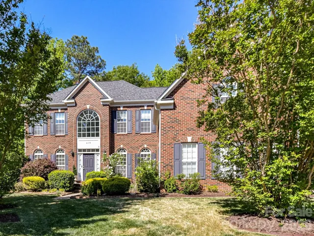 Stately two-story brick home with classic shutters, grand arched entry window, and beautifully landscaped yard offering timeless curb appeal in a serene, tree-lined setting.