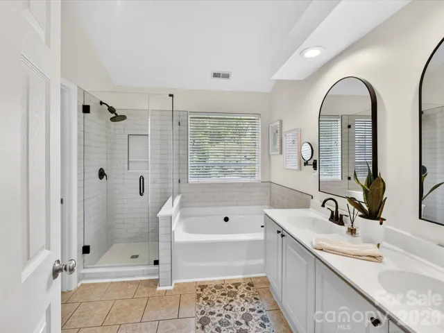 Spa-like primary bath features a dual vanity, soaking tub, and separate glass-enclosed shower with stylish tile finishes and abundant natural light.