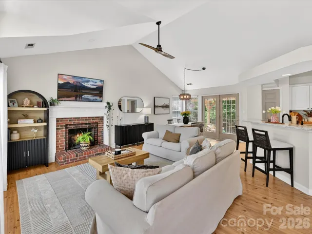 Spacious great room with soaring vaulted ceilings, abundant natural light, and a cozy fireplace seamlessly connecting to the kitchen and dining areas.