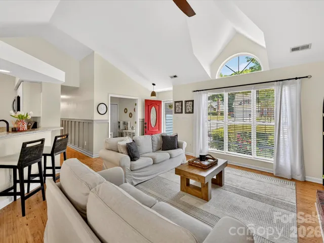 Spacious great room with soaring vaulted ceilings, abundant natural light, and a cozy fireplace seamlessly connecting to the kitchen and dining areas.