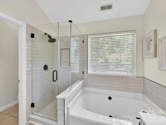 Spa-like primary bath features a dual vanity, soaking tub, and separate glass-enclosed shower with stylish tile finishes and abundant natural light.