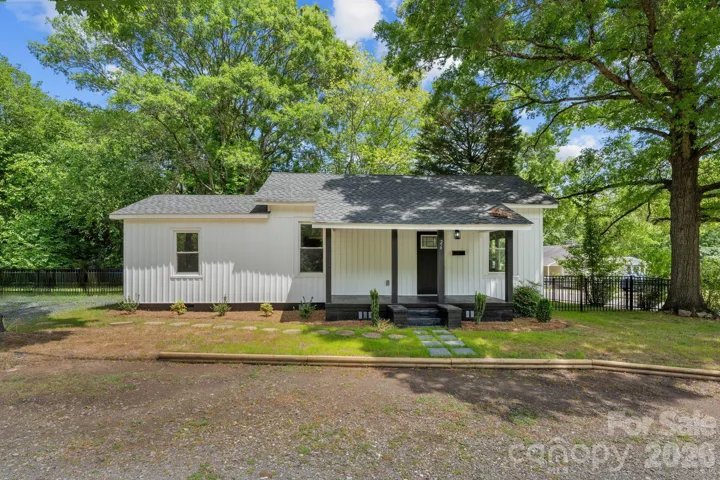 This beautifully renovated modern farmhouse cottage features crisp white vinyl siding perfectly accented by bold black trim and a charming recessed front porch. The high-contrast aesthetic creates a striking curb appeal, nestled against a lush backdrop of mature trees for the perfect blend of style and serenity.