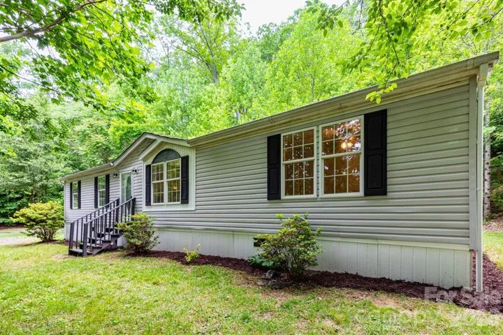Exterior Front – Nestled in a peaceful wooded setting, this well-maintained home offers privacy, mature landscaping, and a welcoming front entrance surrounded by nature.