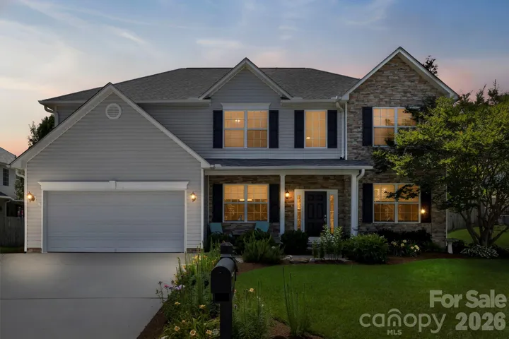 Beautiful two-story home with stone accents, manicured landscaping, and warm interior lighting creating an inviting curb appeal at dusk.