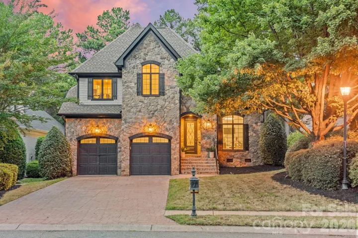 Twilight curb appeal at 17411 Summer Place Drive in The Peninsula, Cornelius NC 28031 - stone and shake exterior, arched double garage, and professional landscape lighting minutes from Lake Norman.