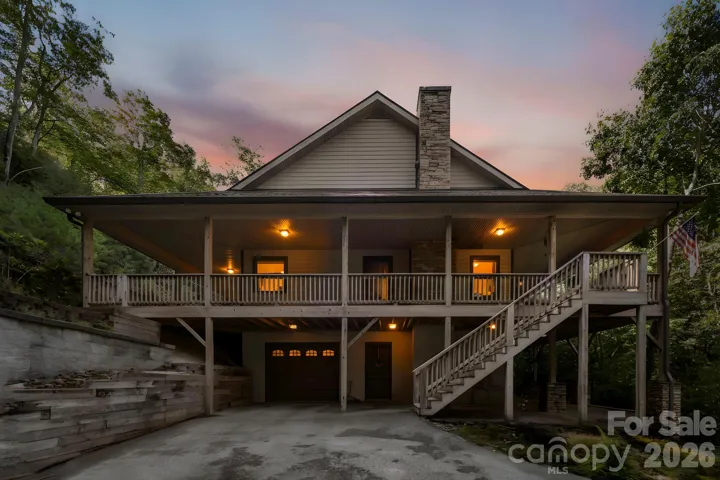 Twilight view showcasing the inviting wraparound porch and striking stone chimney.