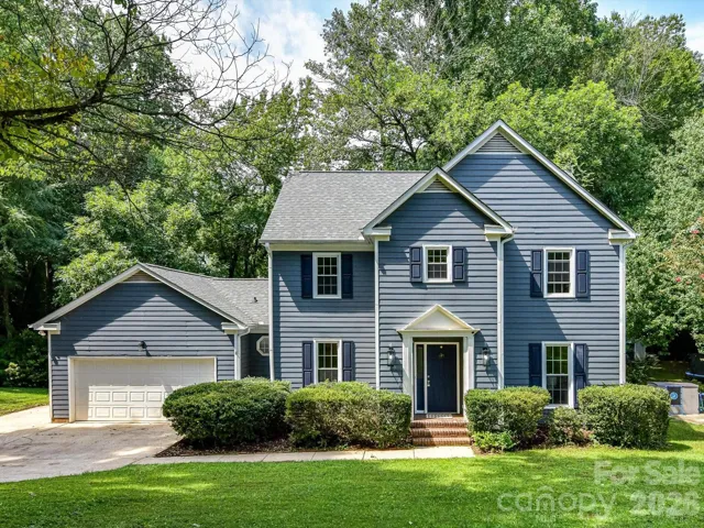 Charming two-story home featuring classic curb appeal, mature landscaping, a spacious front lawn, and an attached two-car garage in a peaceful wooded setting.