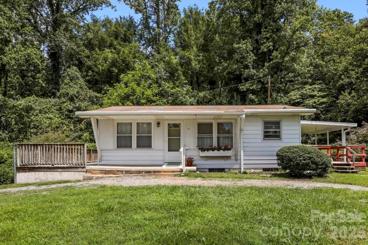 Front exterior view showcasing the single-level home (with basement), welcoming entry, mature landscaping, and wooded surroundings.
